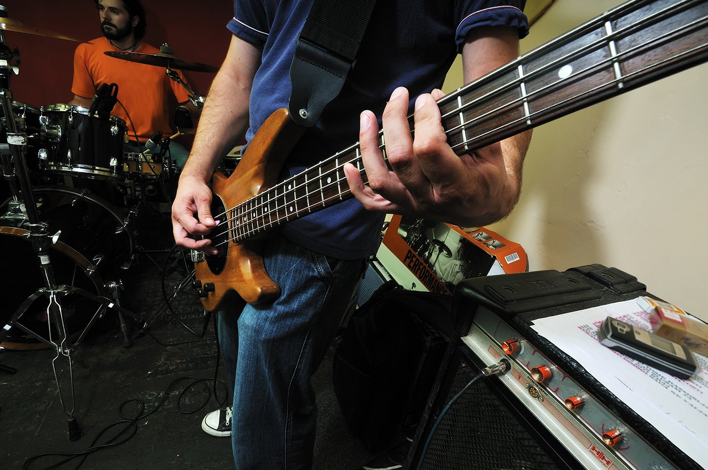 Closeup of bass guitar player performing with drummer in background at Kelowna music lesson.