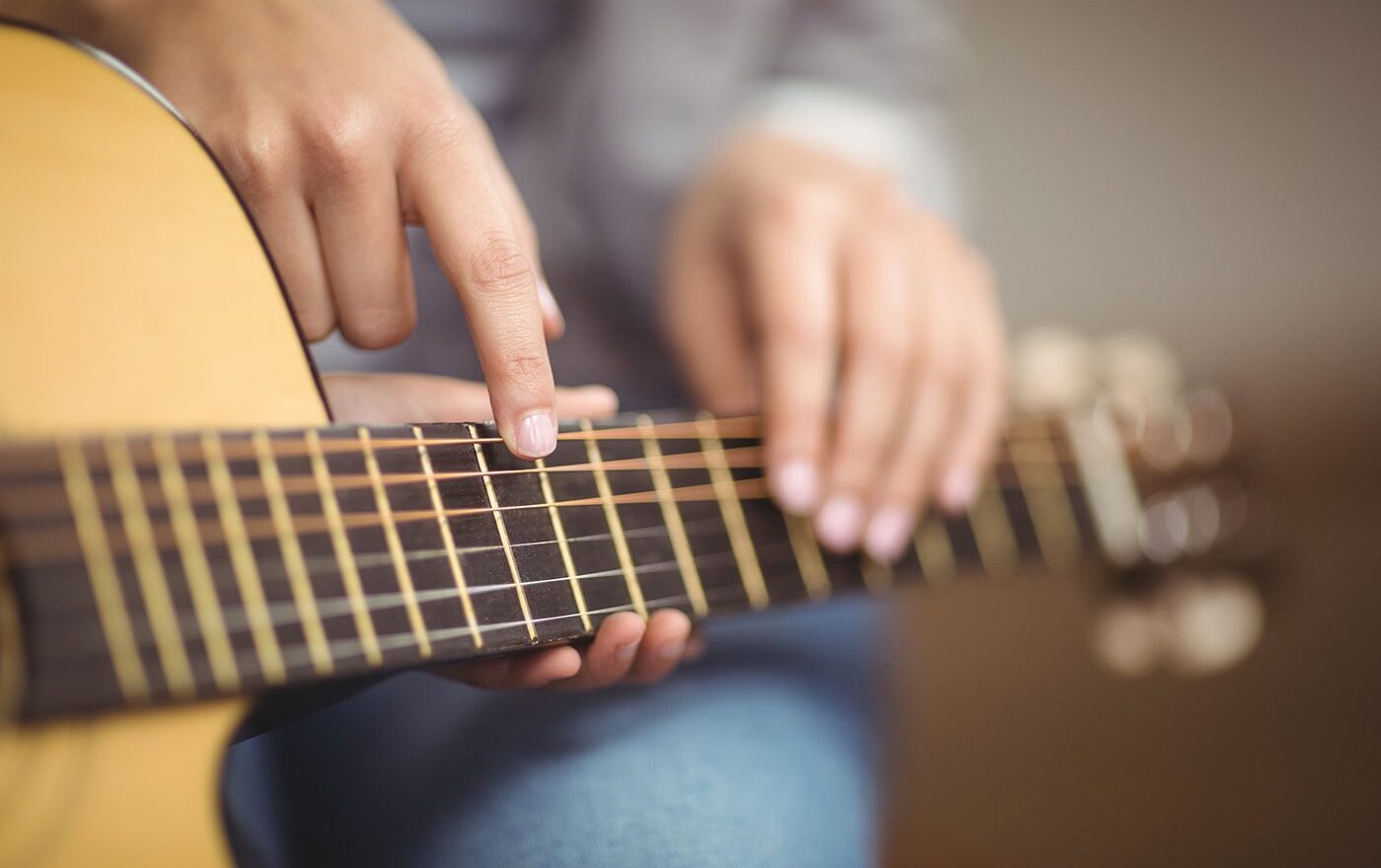 Kelowna guitar teacher giving private lesson, pointing at student’s acoustic guitar during practice.